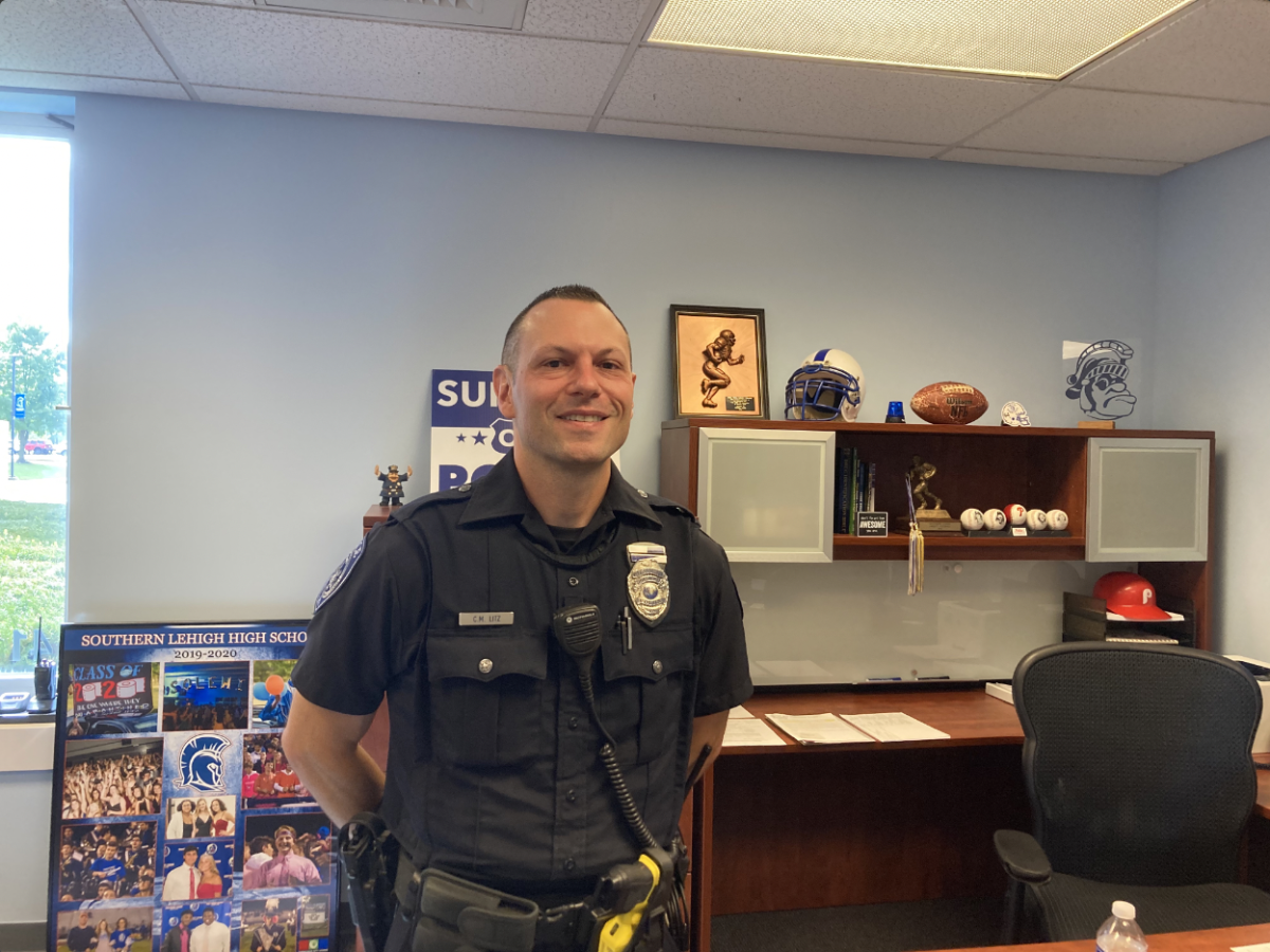 Officer Litz stands in front of his awards and souvenirs from high school football. 